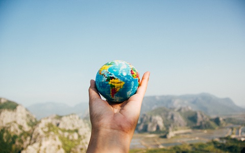 Hand holding small globe with mountains in background